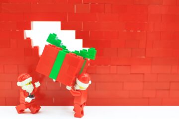 Red and green toy figures carrying a Christmas gift against a red background.