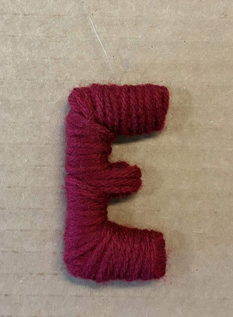 Finished red yarn-wrapped letter E ornament with a fishing-line hanging loop